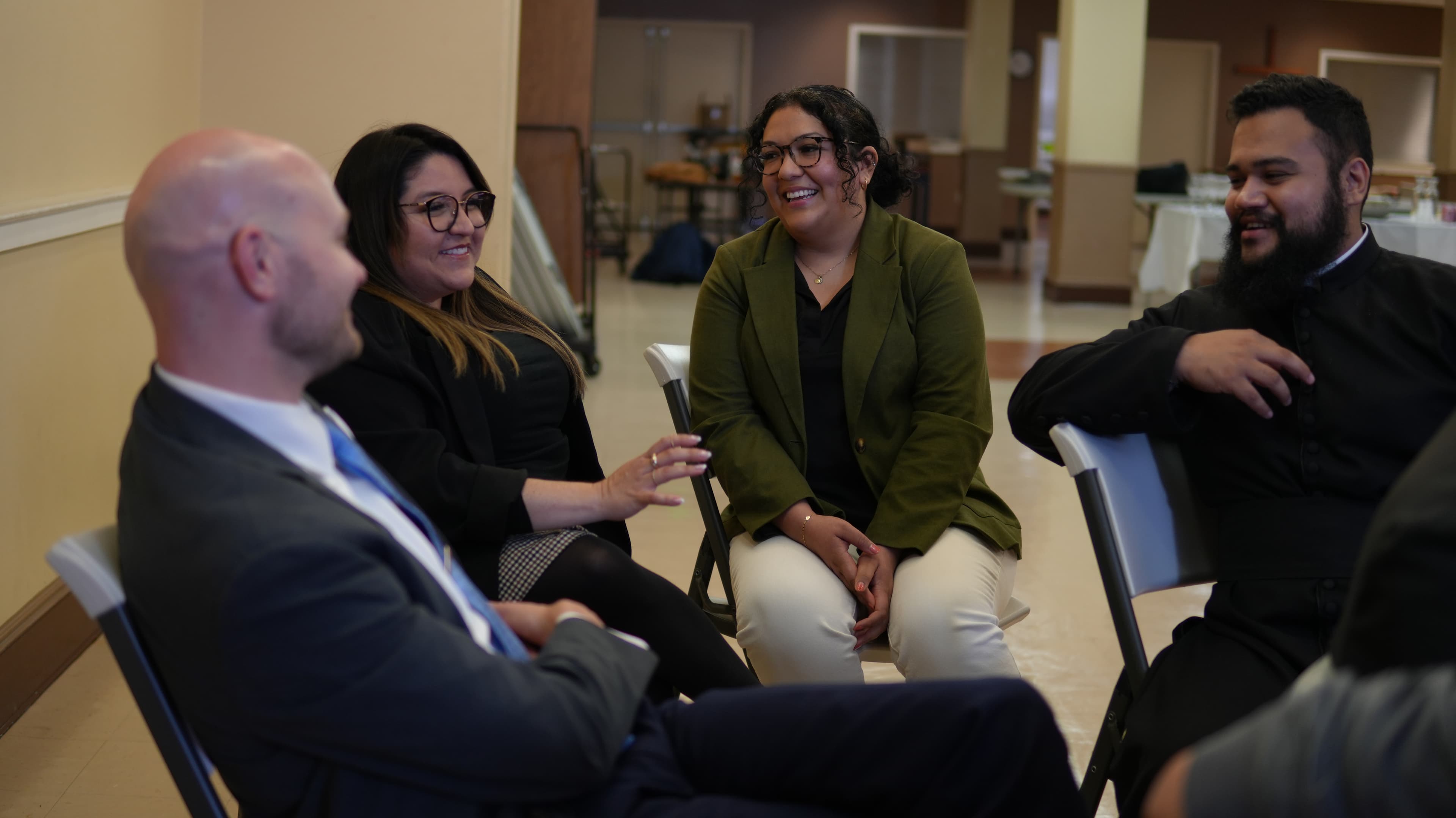 Four people seated in a circle, smiling and talking during a community gathering