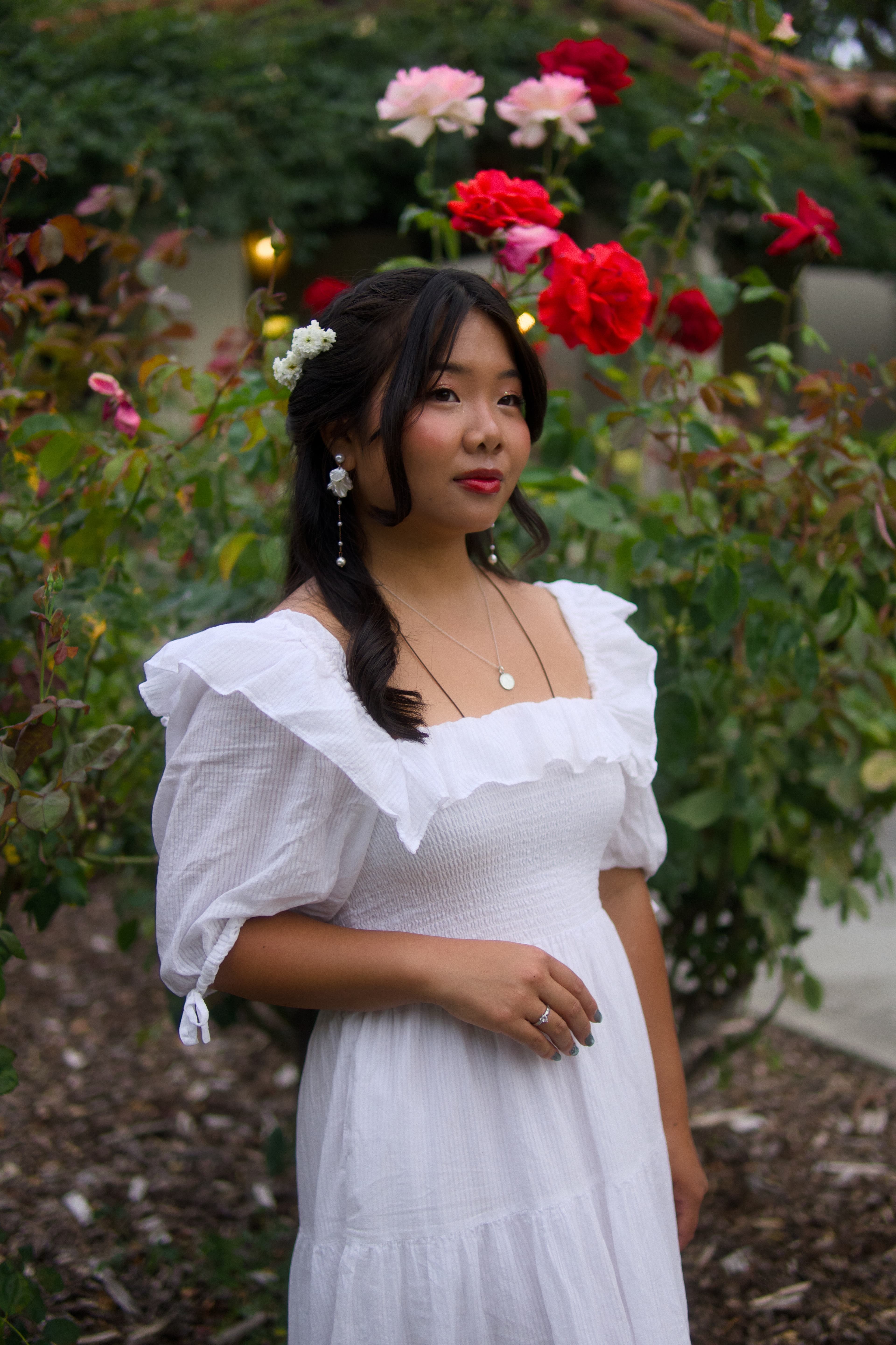 A woman in a white dress standing beneath red and pink roses along a garden path