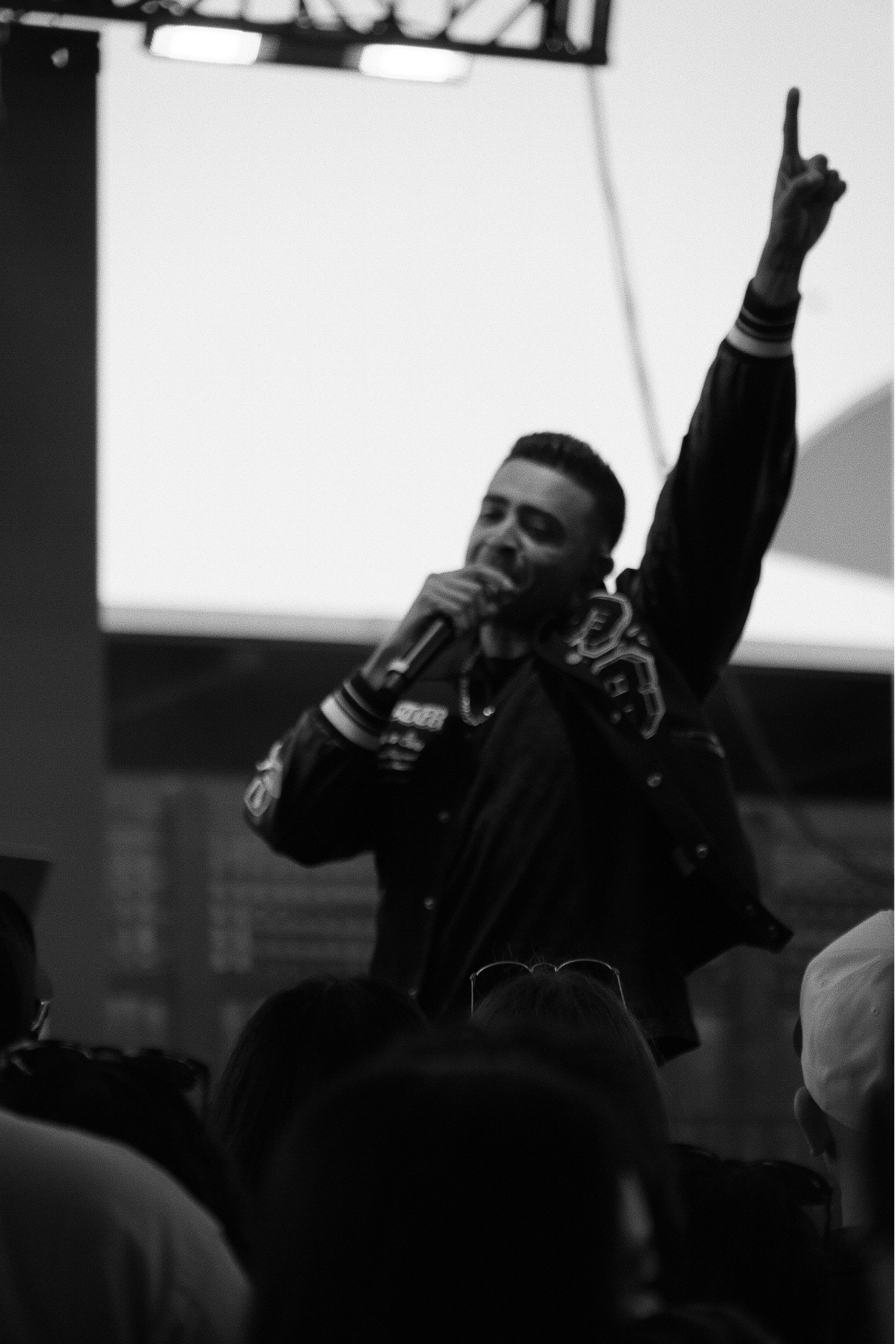 Black-and-white photograph of a speaker holding a microphone and raising one hand above the audience